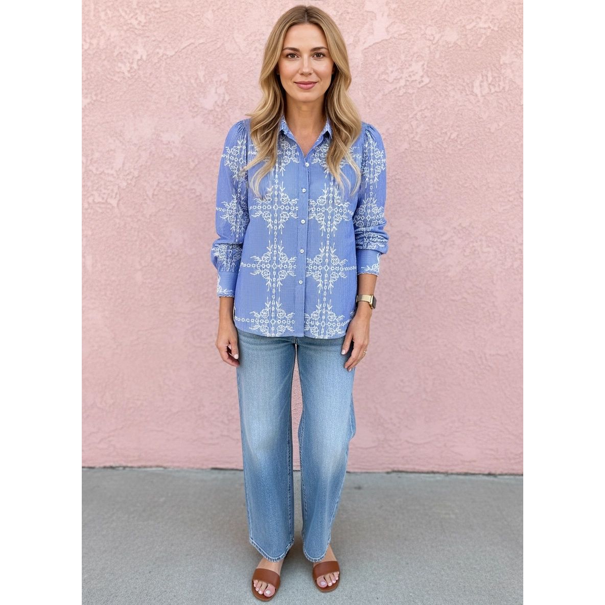 Woman wearing a blue patterned shirt and jeans against a pink wall.