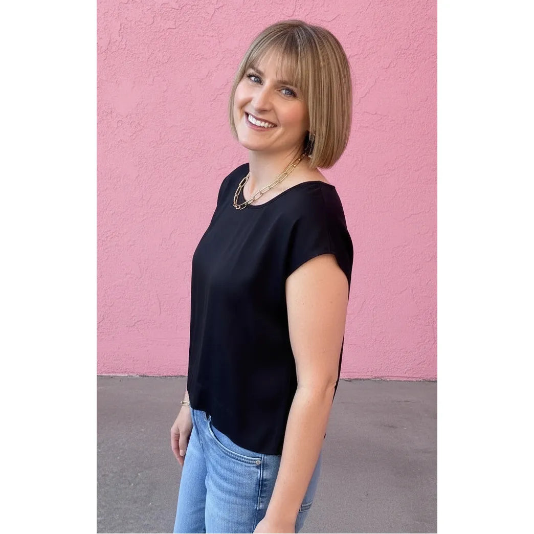 Woman in a black top and blue jeans standing against a pink wall