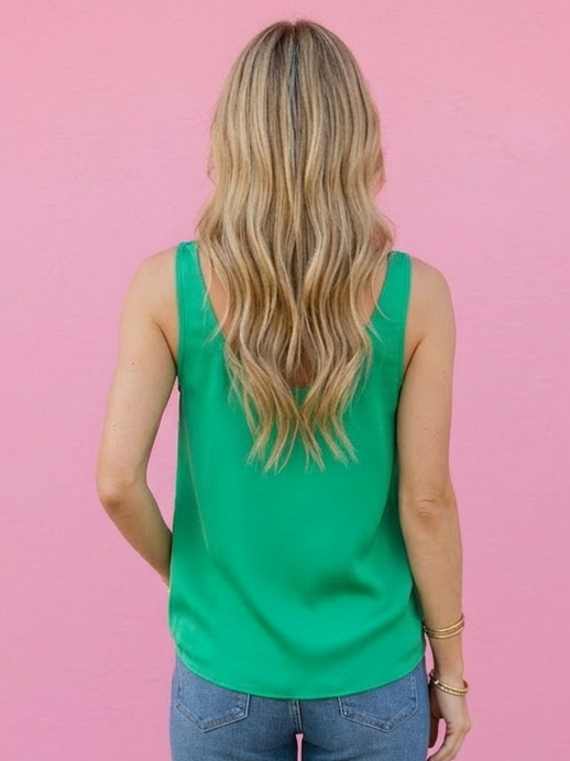 Person wearing a green sleeveless top and blue jeans against a pink wall.