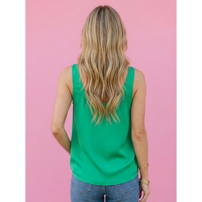 Person wearing a green sleeveless top and blue jeans against a pink wall.