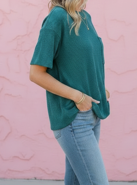 Woman wearing a teal top and blue jeans against a pink wall