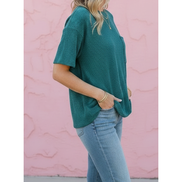 Woman wearing a teal top and blue jeans against a pink wall