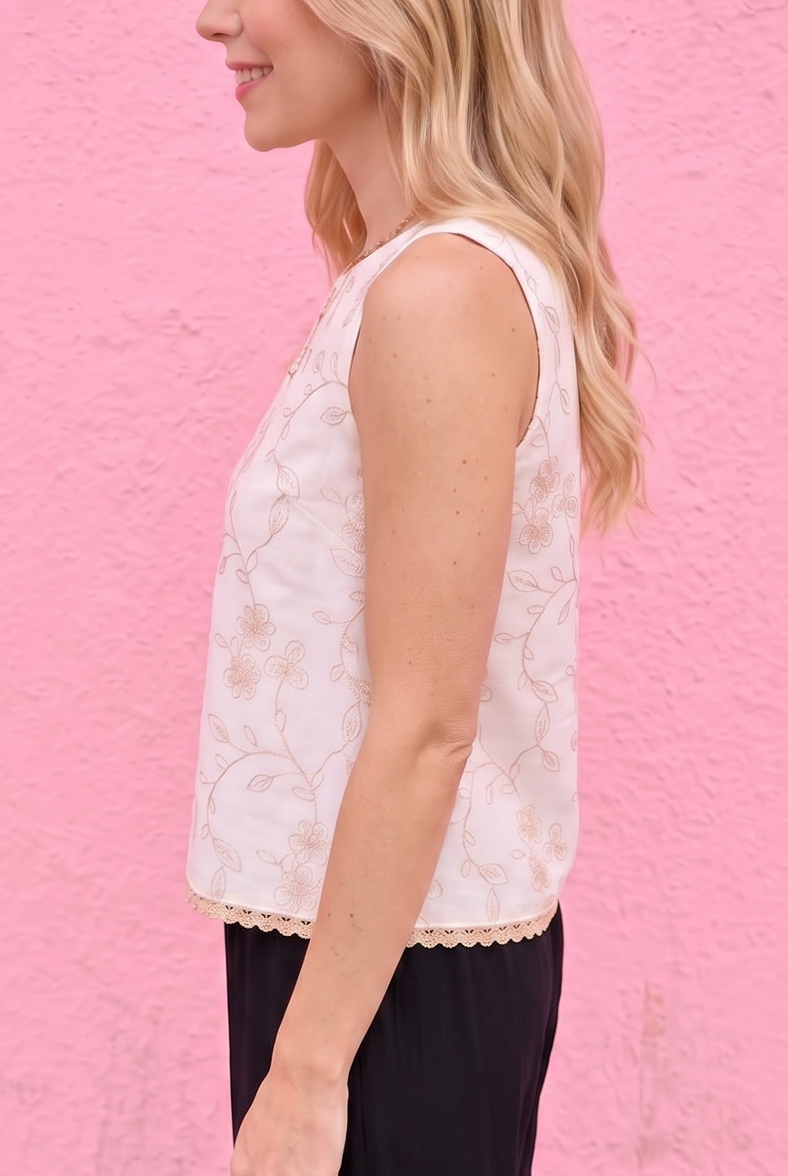 Woman wearing a white sleeveless top and black pants against a pink wall.