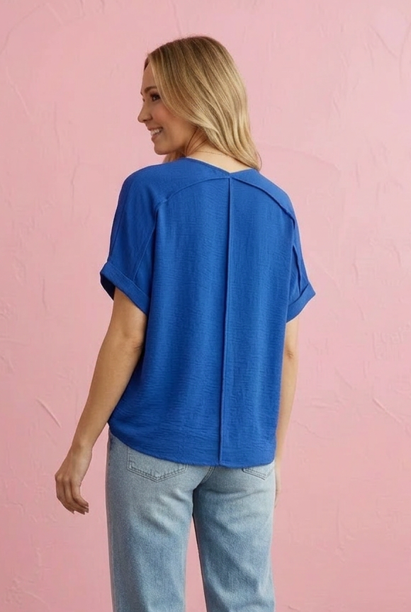 Woman wearing a blue top and light blue jeans against a pink wall.