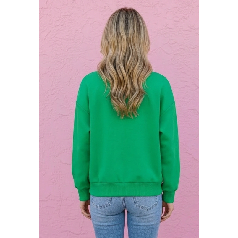 Person wearing a green sweatshirt and blue jeans standing against a pink wall.