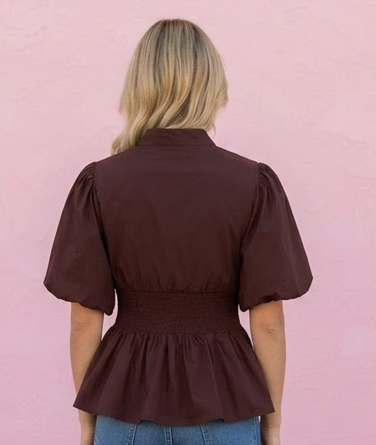 Person wearing a brown peplum top and blue jeans against a pink wall.