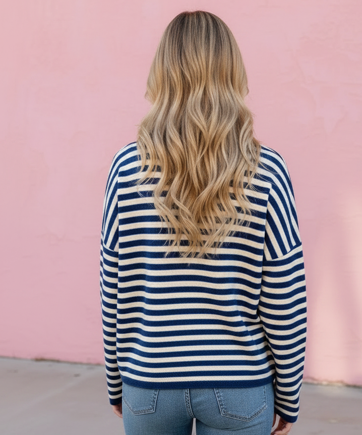 A woman viewed from behind wearing a navy and white horizontally striped long-sleeve top and light blue jeans, standing against a solid pink wall.