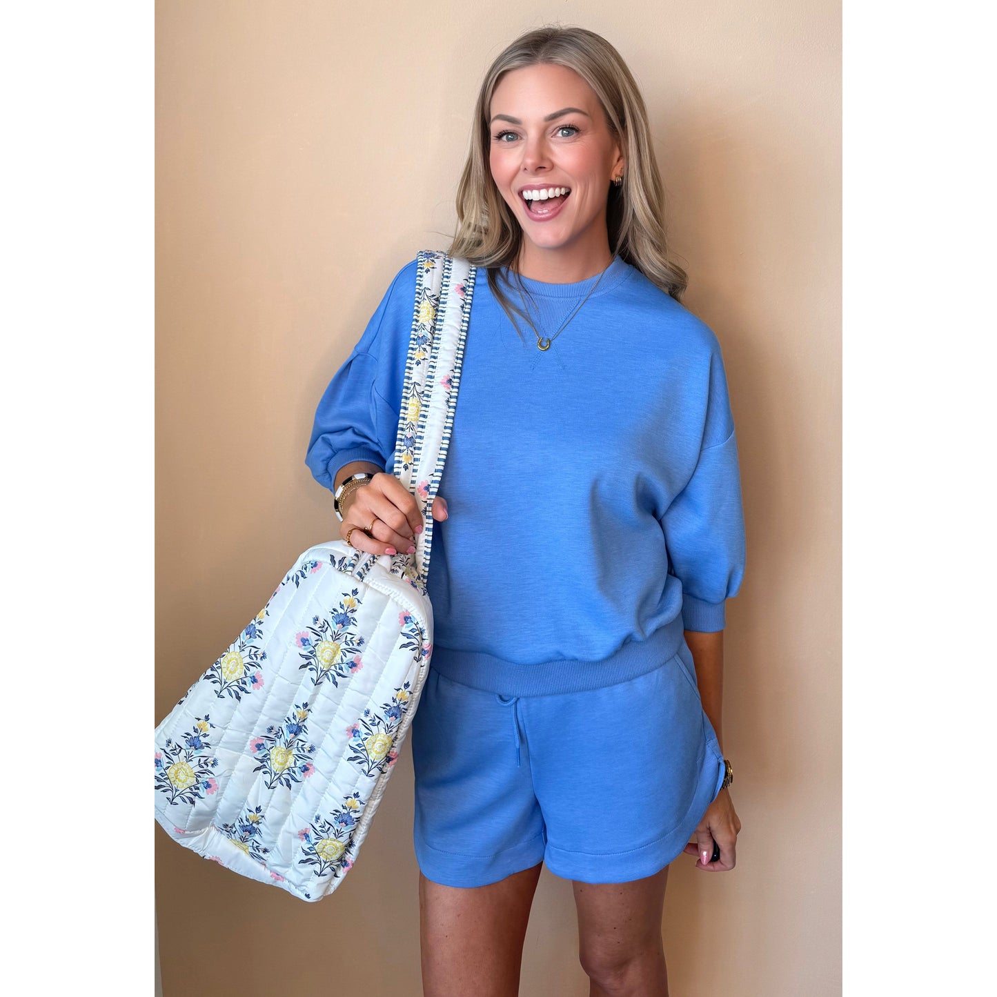 Woman in blue outfit holding a floral bag against a beige background