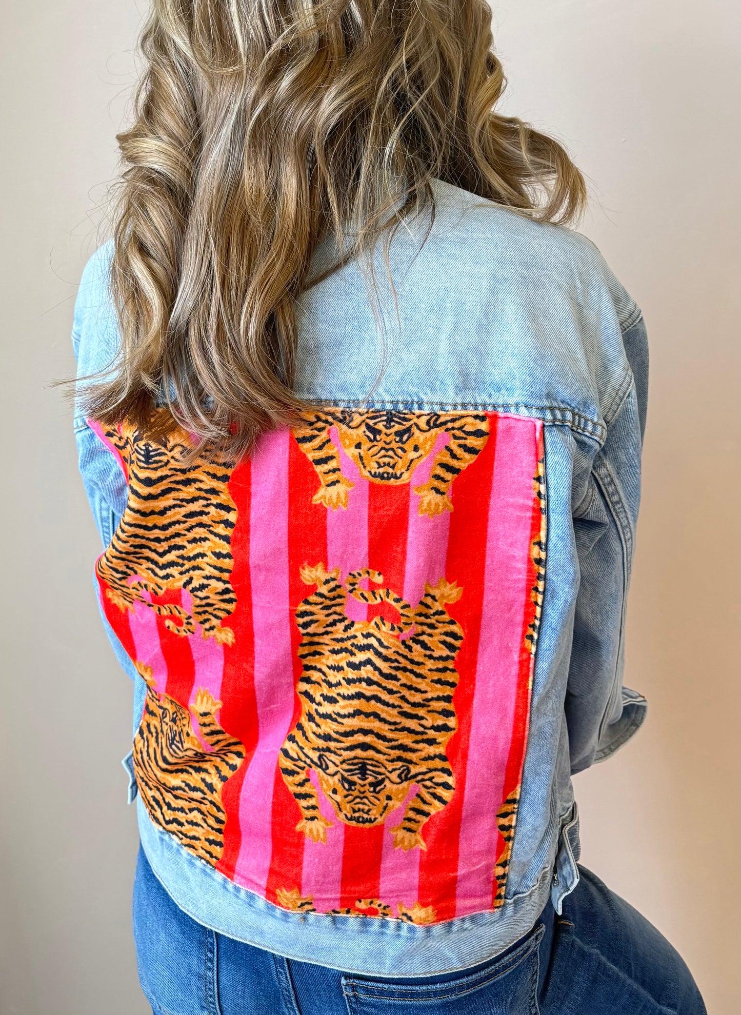 Denim jacket with tiger print panel on a plain background