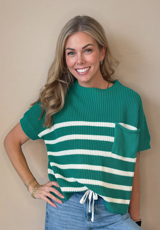 Woman wearing a green and white striped sweater and blue jeans against a beige wall.