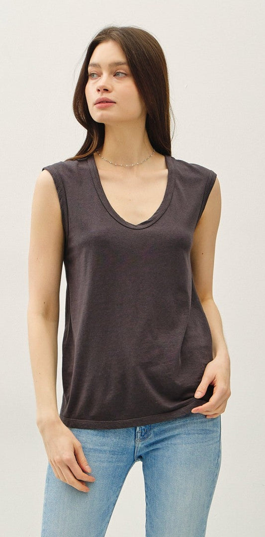 Woman wearing a dark sleeveless top and light blue jeans against a white background