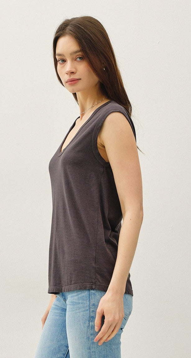 Woman wearing a dark sleeveless top and light blue jeans against a white background