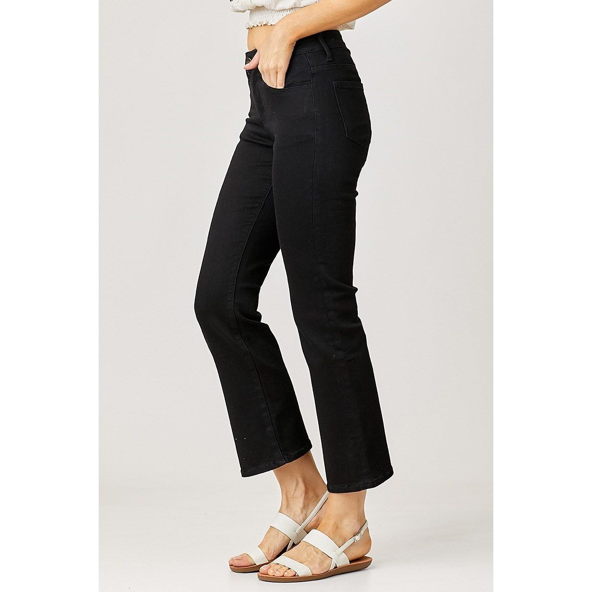 Person wearing black risen jeans and white sandals on a plain background