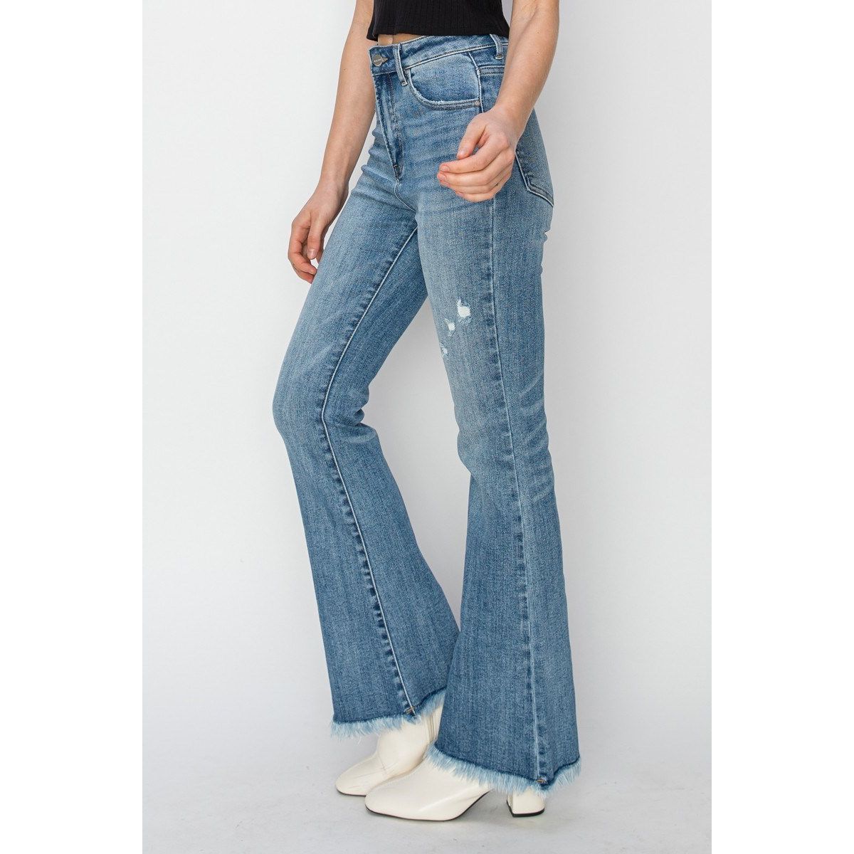 Woman wearing a black top and blue jeans with a frayed hem against a white background 