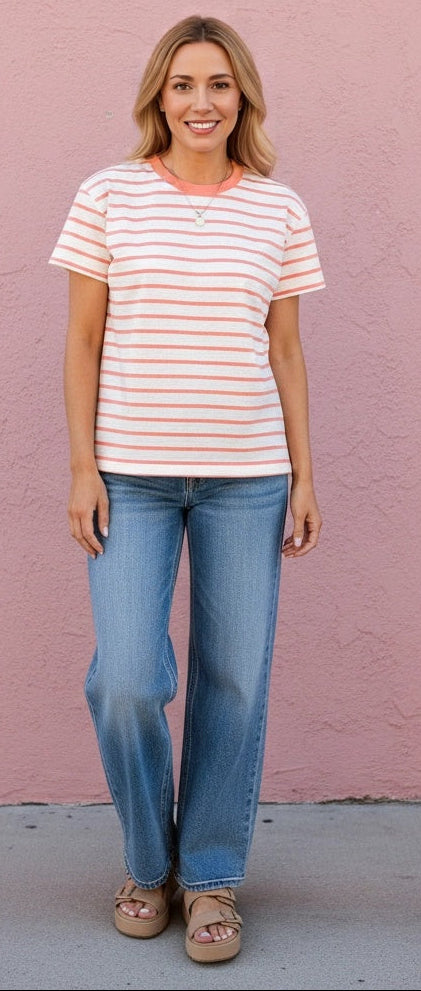 Woman wearing a striped shirt and jeans standing against a pink wall