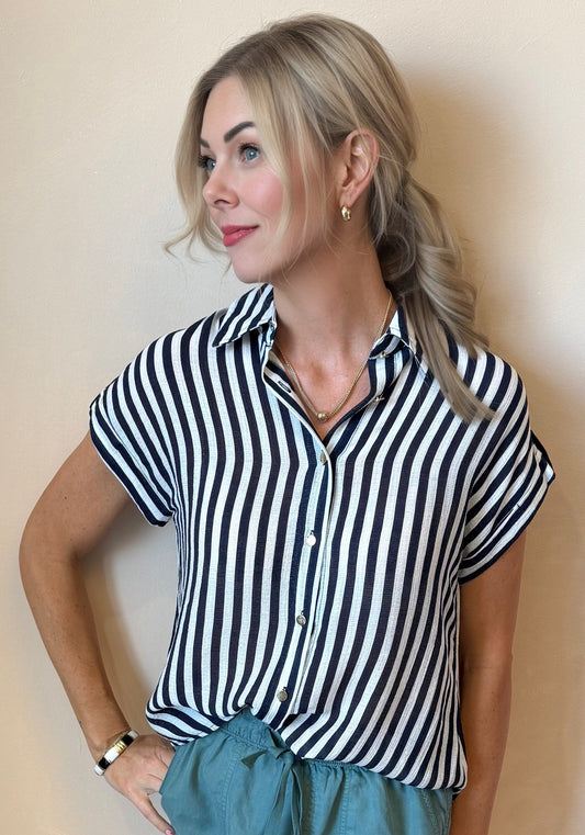 Woman wearing a black and white striped shirt and teal shorts against a beige wall.