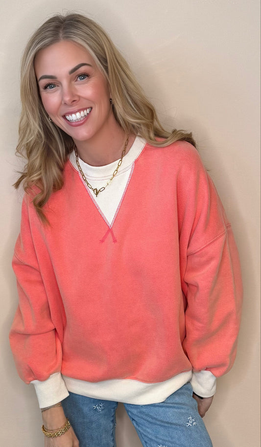 Woman wearing a coral sweater over a white shirt with blue jeans against a beige background