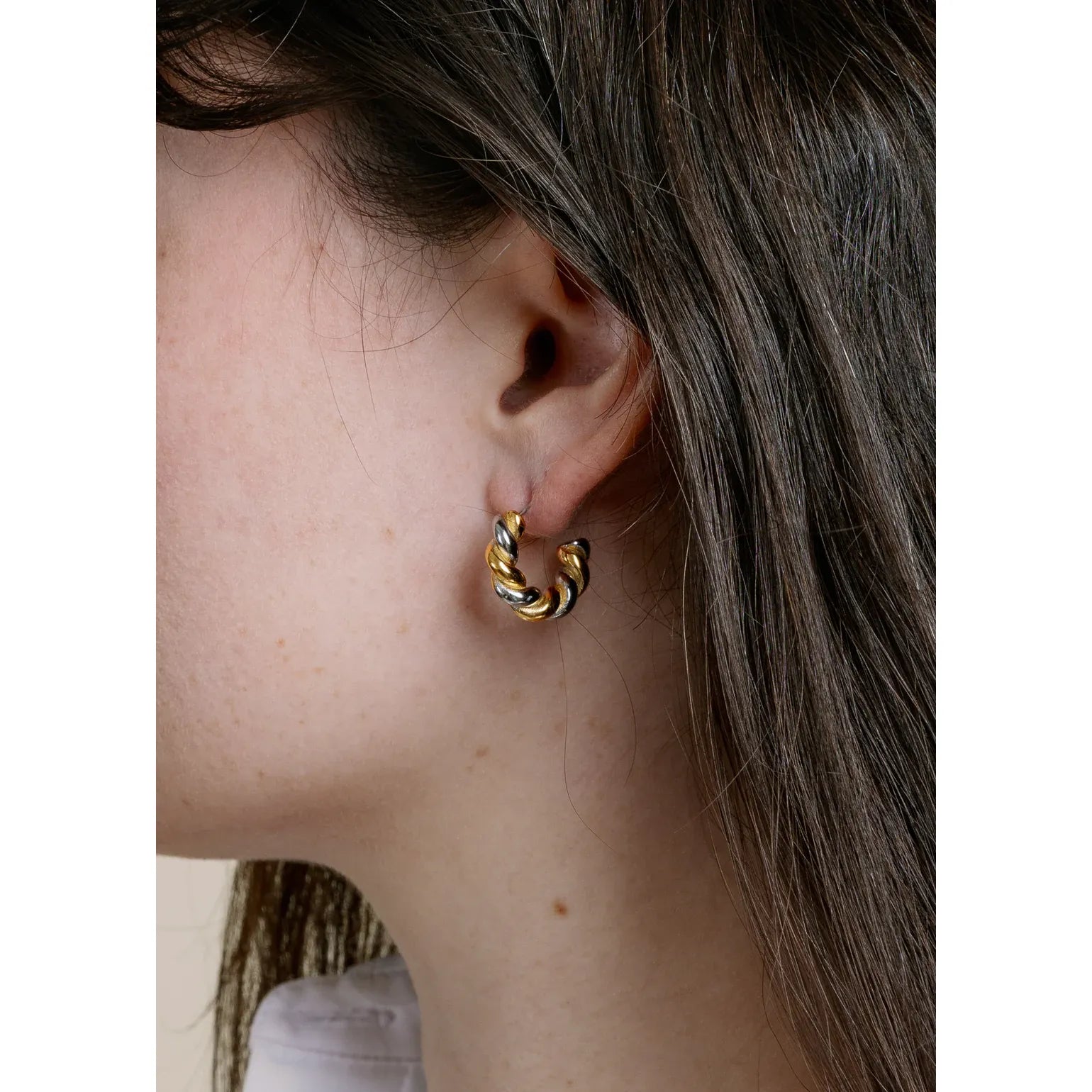 Close-up of a person wearing a gold hoop earring with a blurred background