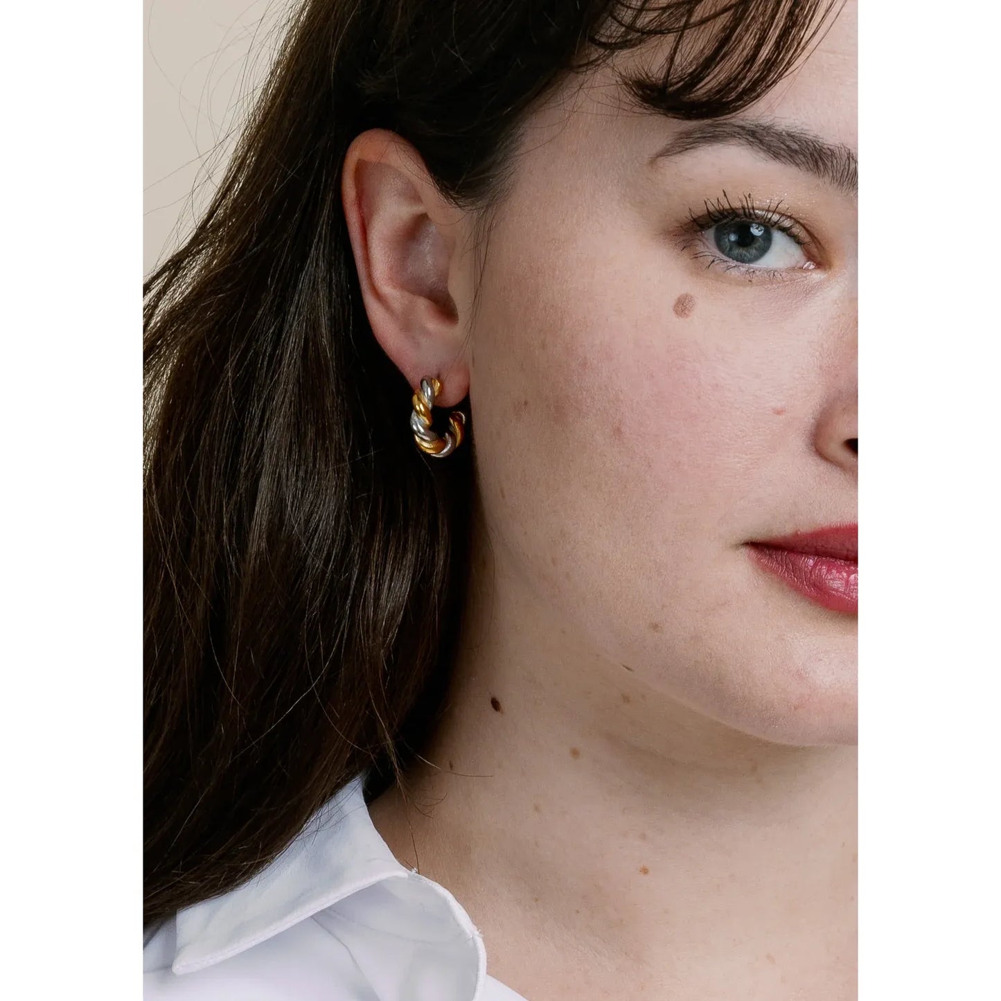Close-up of a person wearing gold hoop earrings with a neutral background