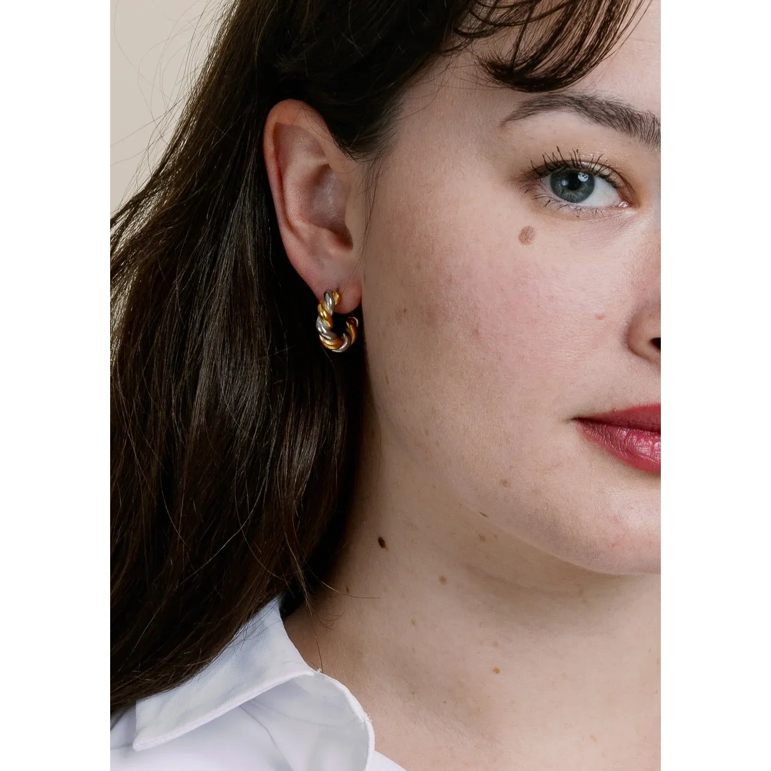 Close-up of a person wearing gold hoop earrings with a neutral background