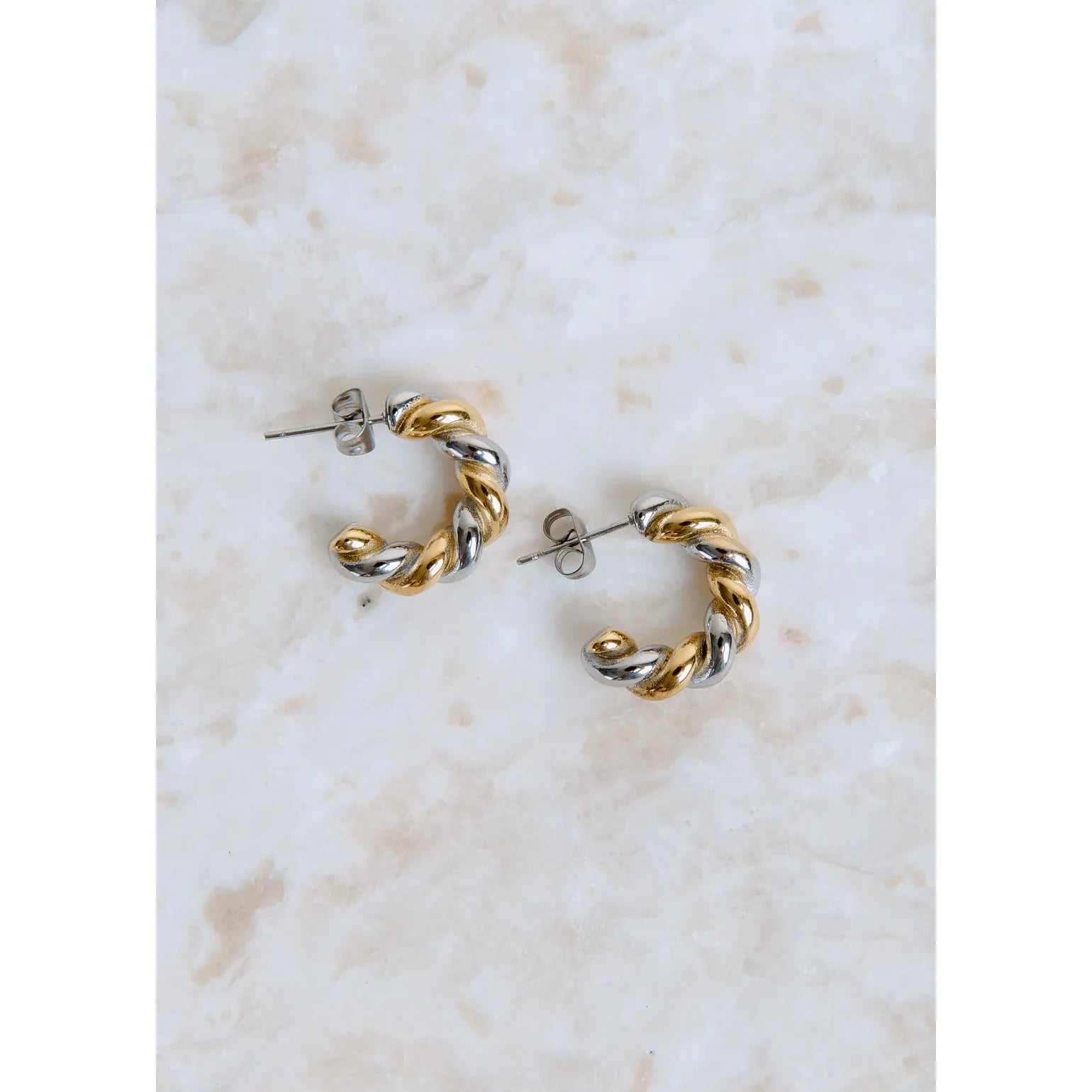 Pair of gold and silver hoop earrings on a marble surface