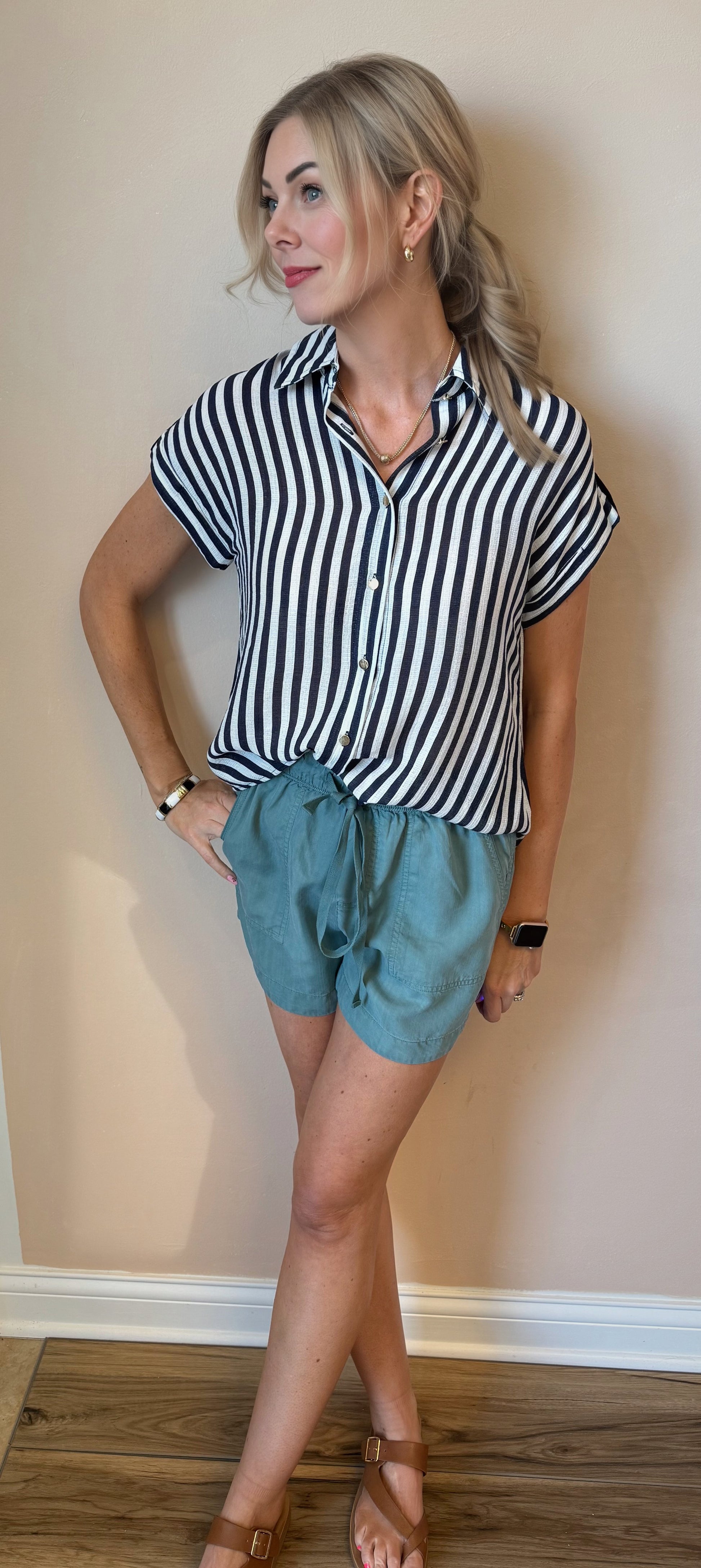 Woman wearing a black and white striped shirt and teal shorts against a beige wall.