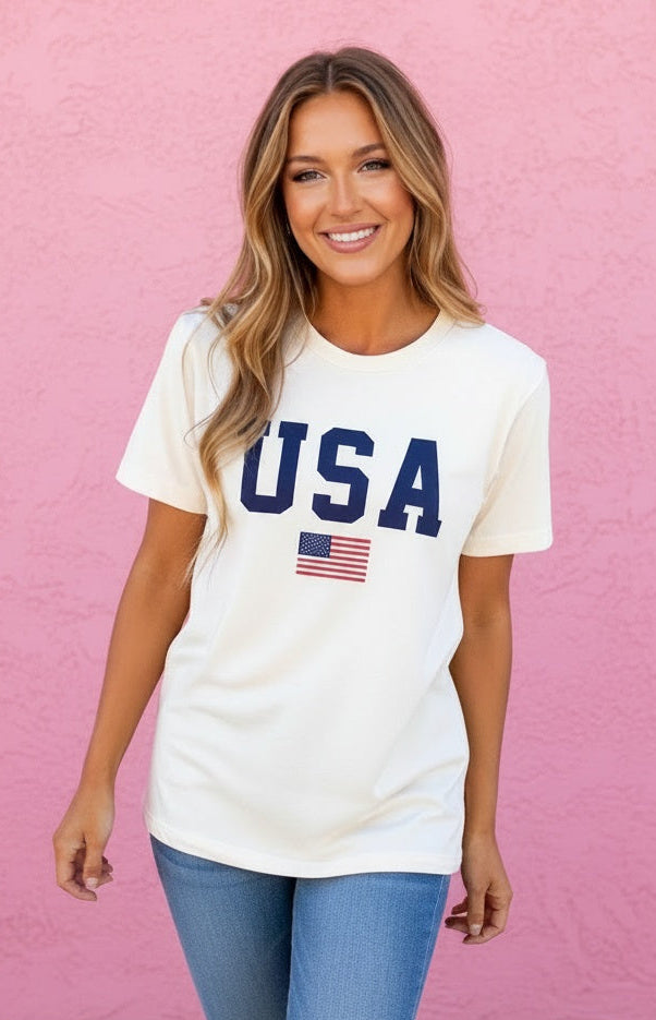 Woman wearing a white 'USA' t-shirt with an American flag against a pink wall