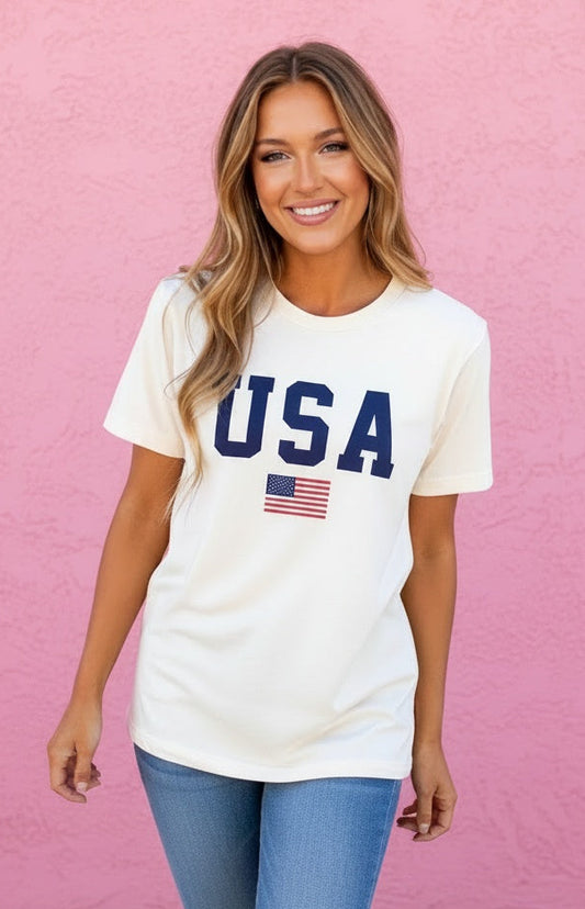 Woman wearing a white 'USA' t-shirt with an American flag against a pink wall