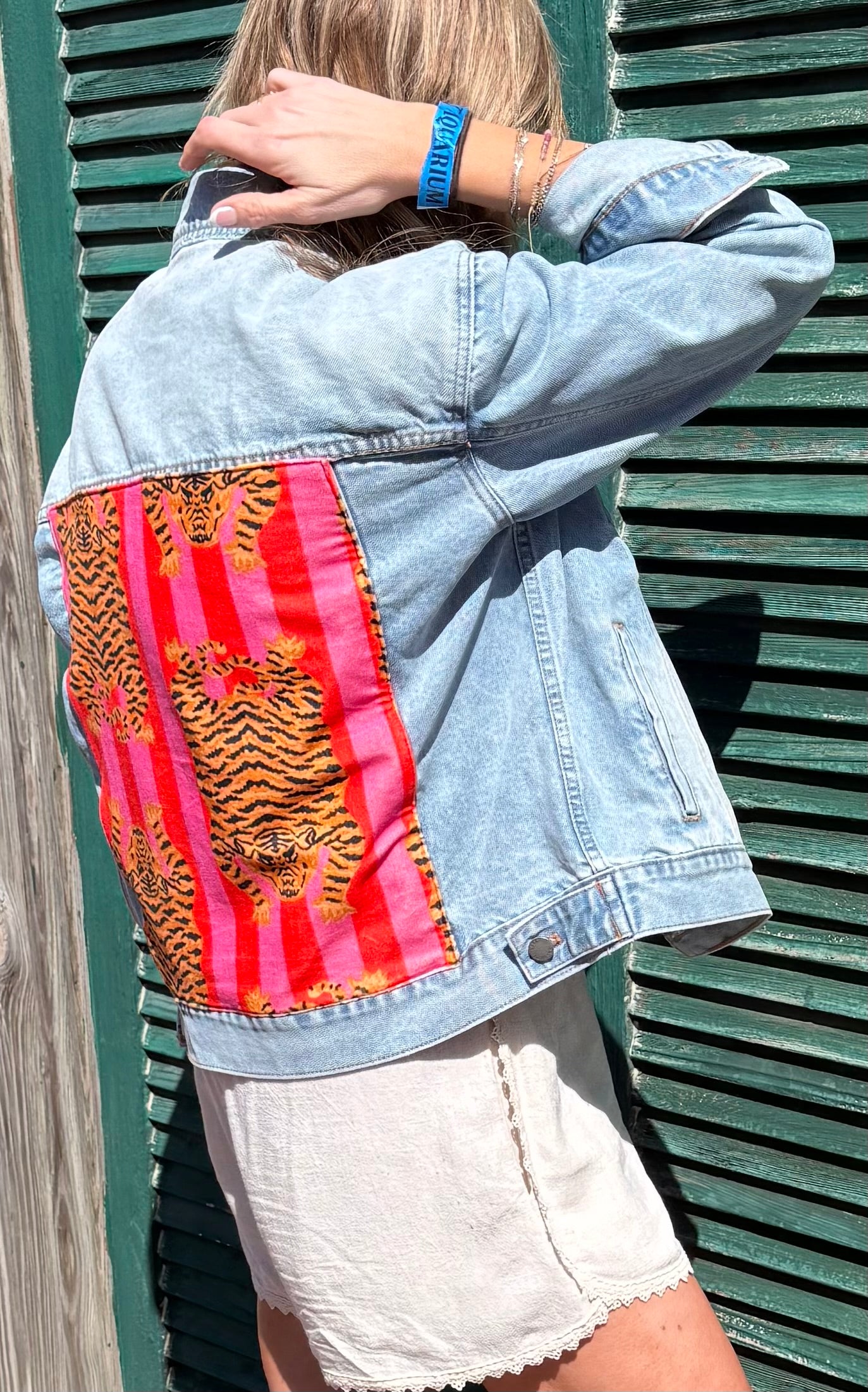 Person wearing a denim jacket with a tiger print panel against a green wooden background