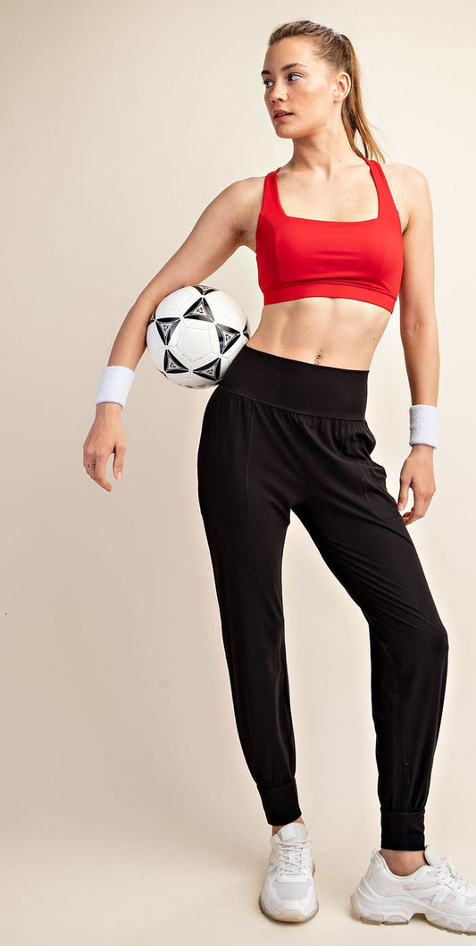 Woman in red sports bra and black pants holding a soccer ball on a beige background