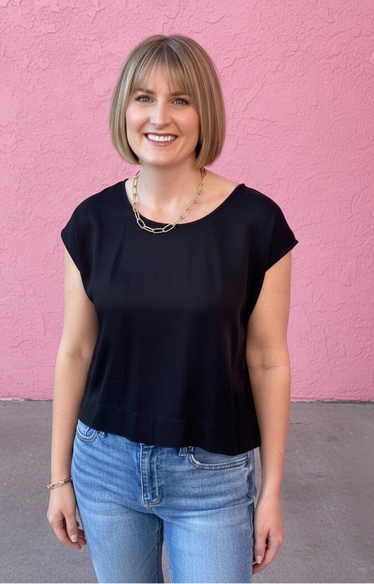 Woman wearing a black top and blue jeans standing against a pink wall