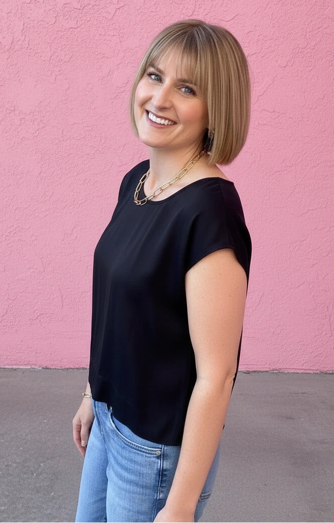 Woman in a black top and blue jeans standing against a pink wall