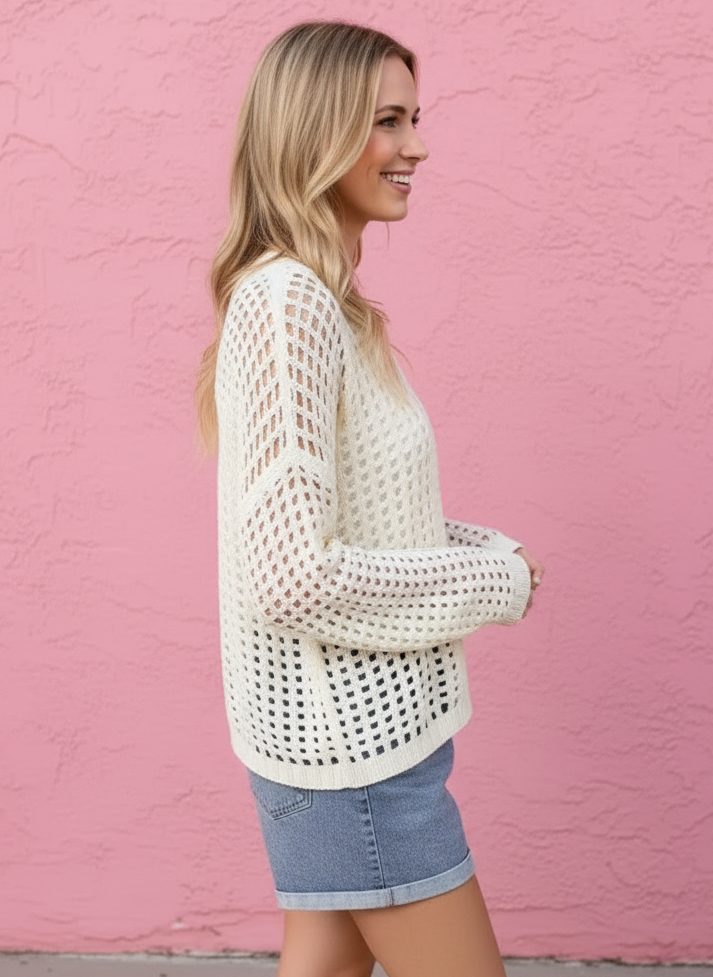 Woman wearing a white mesh top and denim shorts against a pink wall