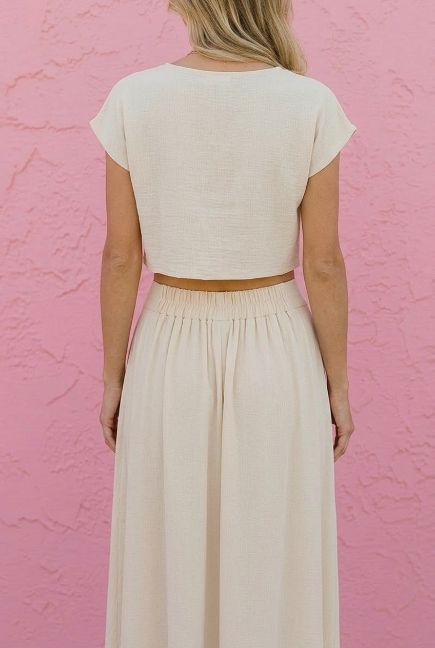 Person wearing a white crop top and long skirt against a pink textured wall