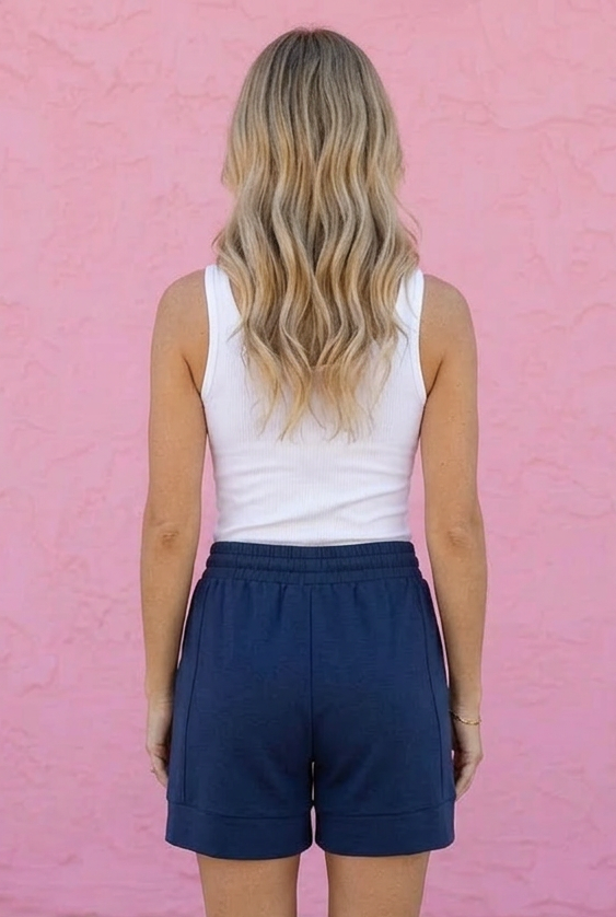 Person wearing navy shorts and a white tank top against a pink wall
