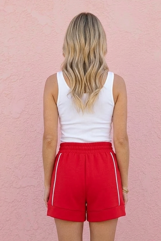 Person wearing red shorts and a white top against a pink wall
