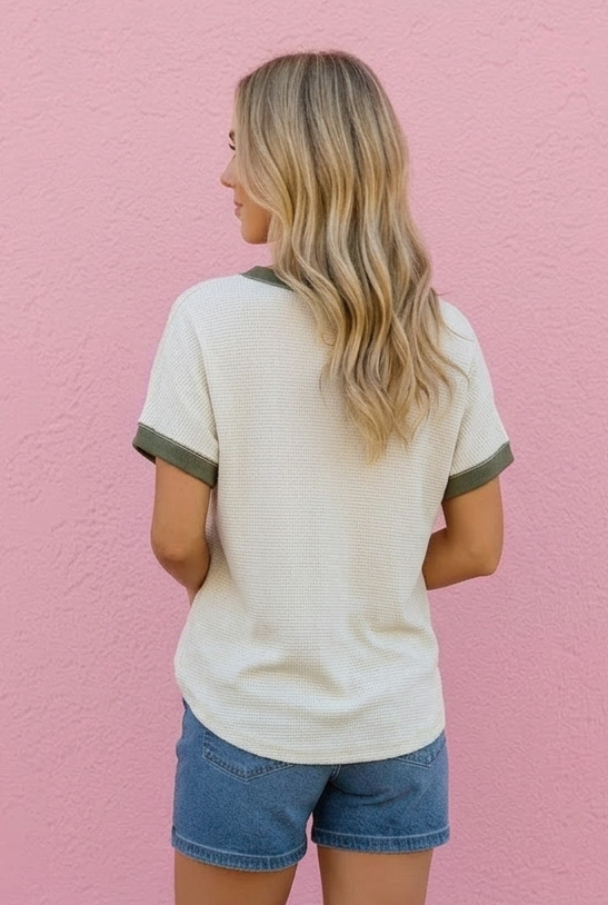 Woman wearing a white t-shirt with green trim and denim shorts against a pink wall.