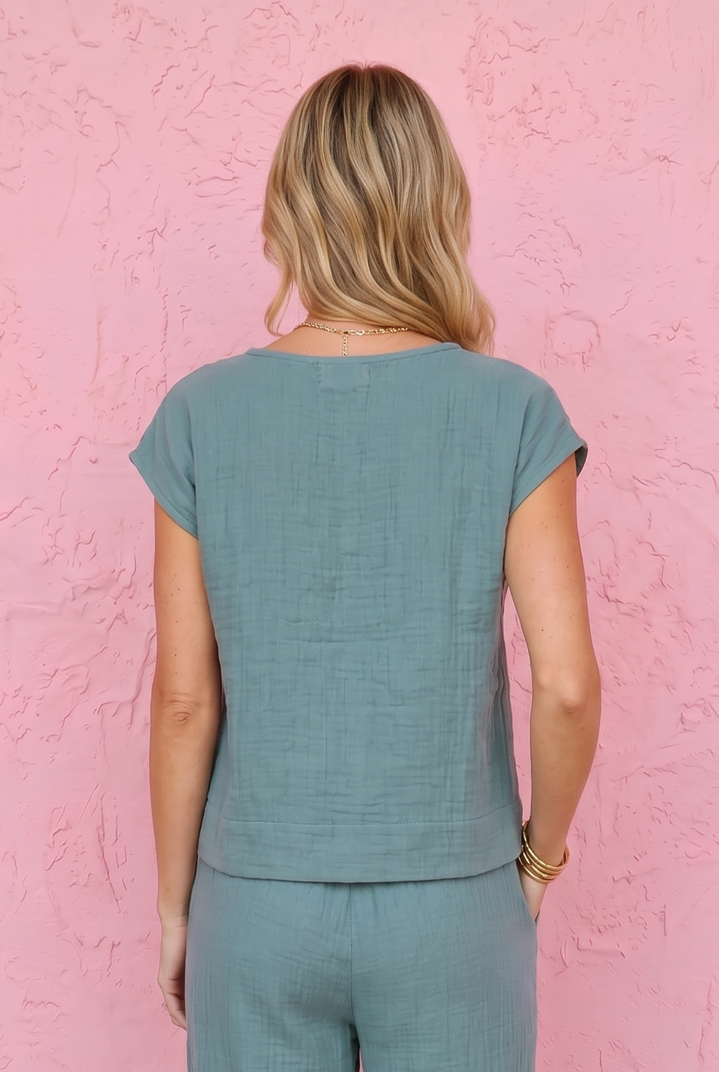 Woman wearing a teal outfit standing against a pink textured wall.