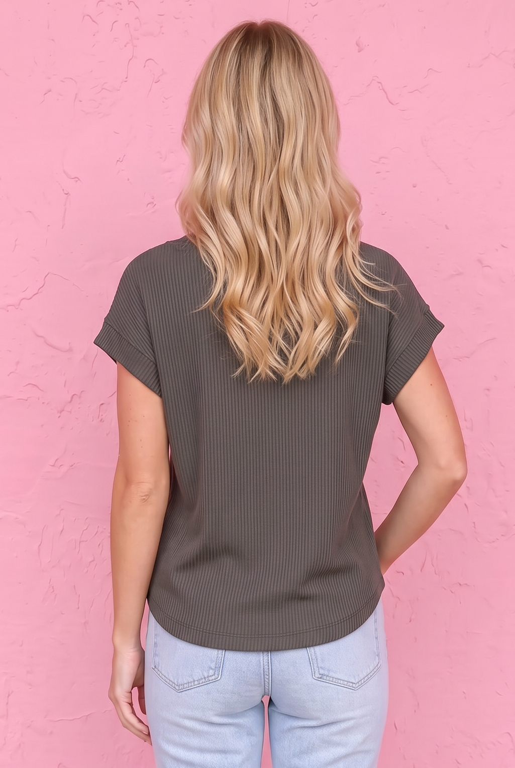 Woman wearing a brown t-shirt and light blue jeans against a pink wall