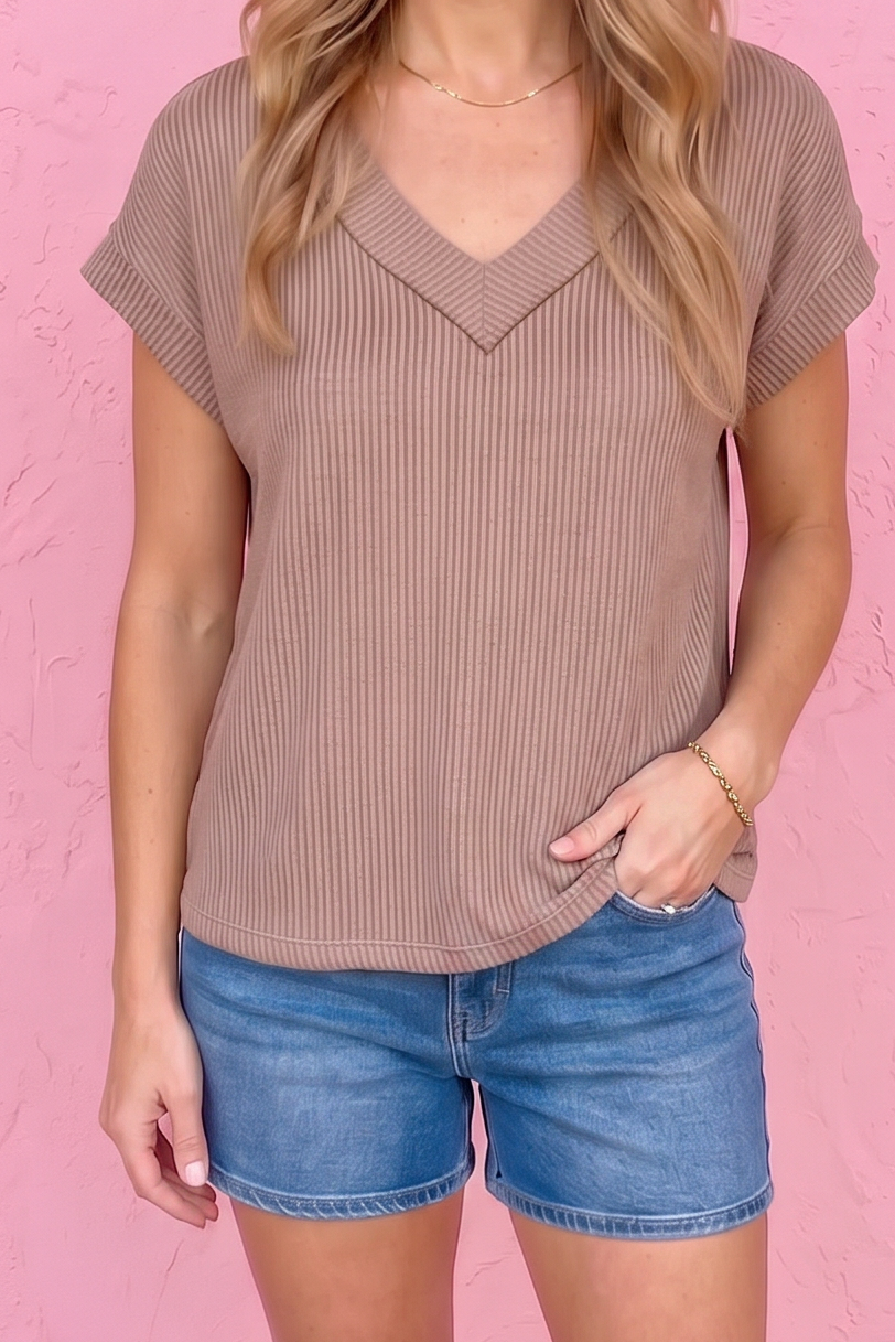 Woman wearing a brown ribbed top and blue denim shorts against a pink wall.