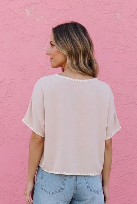Woman wearing a light pink top and denim shorts against a pink wall.