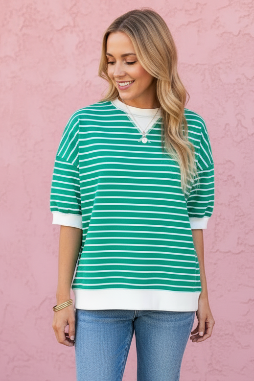 Woman wearing a green and white striped shirt with blue jeans against a pink wall.