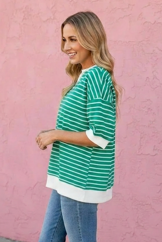 Woman wearing a green and white striped shirt and blue jeans against a pink wall.