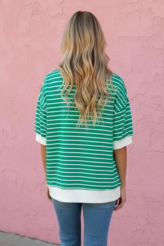 Person wearing a green and white striped shirt and blue jeans standing against a pink wall.