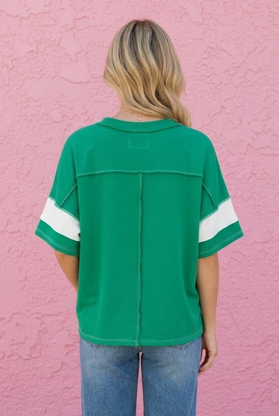 Person wearing a green jersey with white stripes and blue jeans standing against a pink wall.