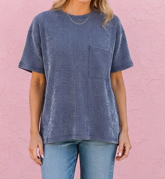 Woman wearing a blue textured t-shirt and jeans standing against a pink wall.