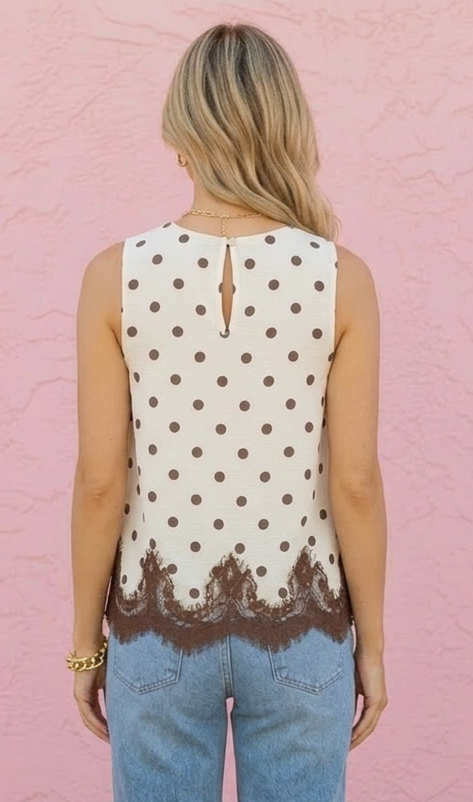 Person wearing a polka dot sleeveless top and blue jeans against a pink wall.