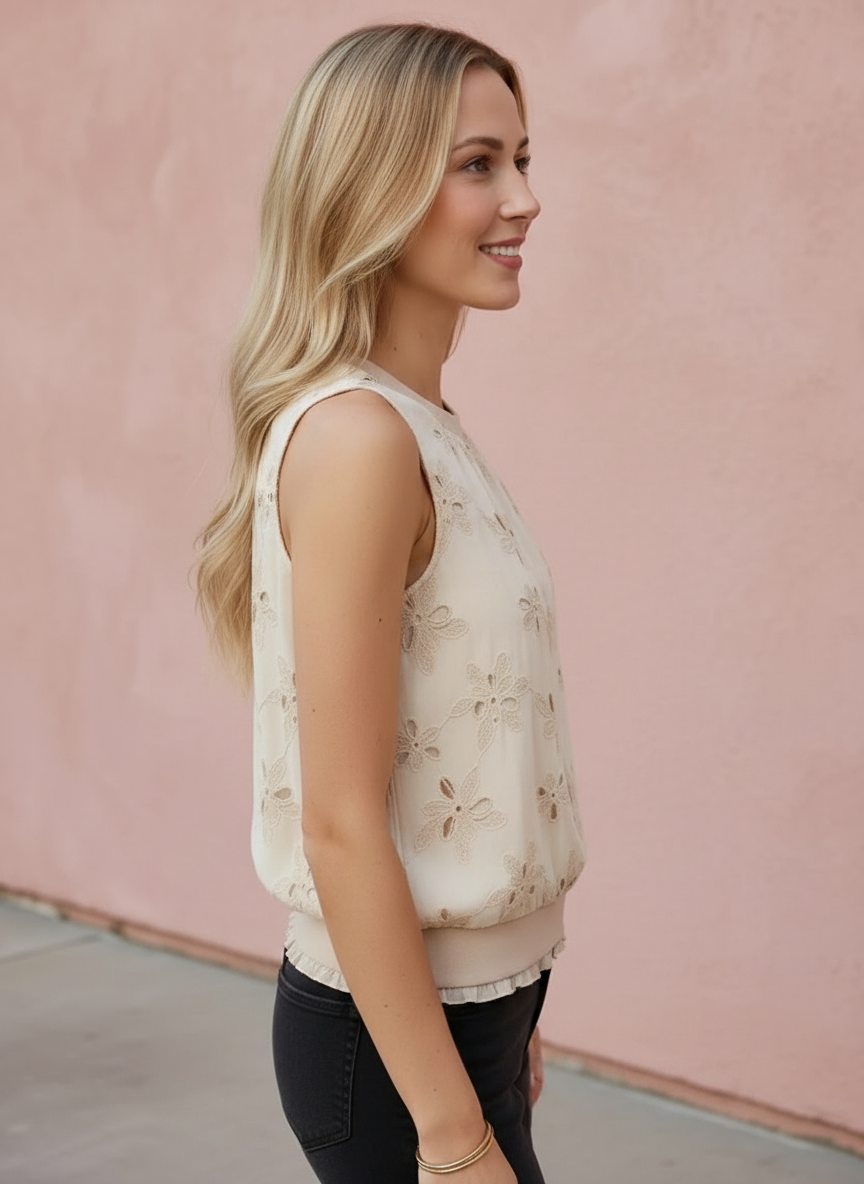 Woman wearing a light-colored sleeveless top with floral patterns against a pink wall.