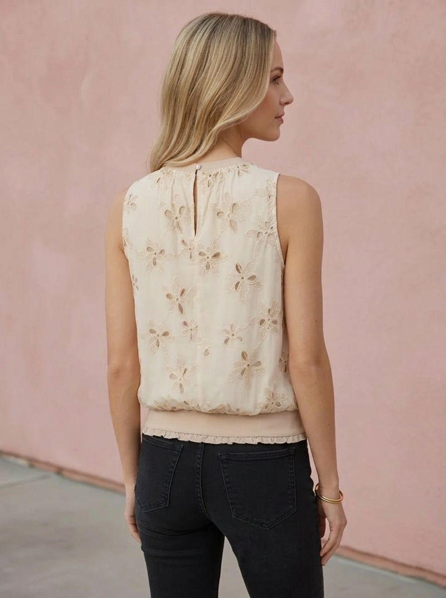 Woman wearing a beige sleeveless top with floral patterns against a pink wall.