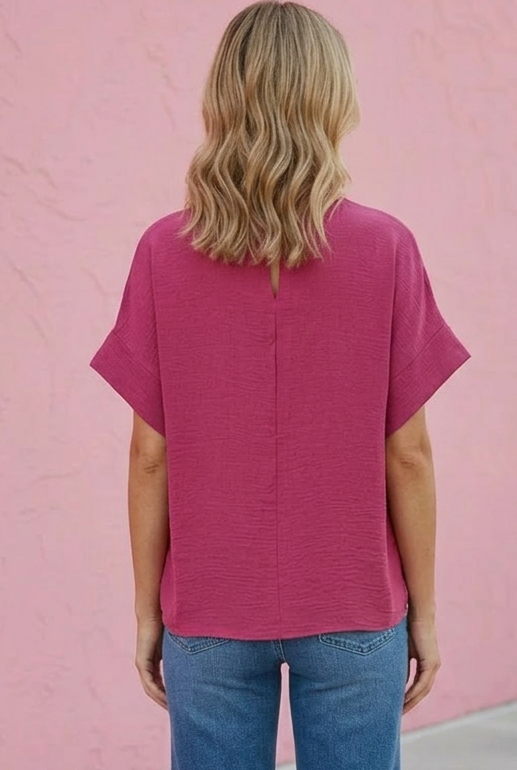 Person wearing a pink top and blue jeans against a pink wall.